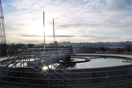 Close-up of a secondary clarifier at the wastewater treatment plant with the sun setting over mountains in the background 