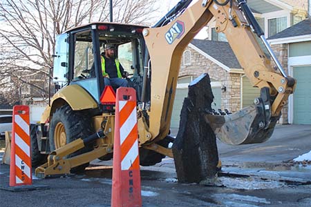 Man operating a backhoe digging up asphalt in the middle of a street