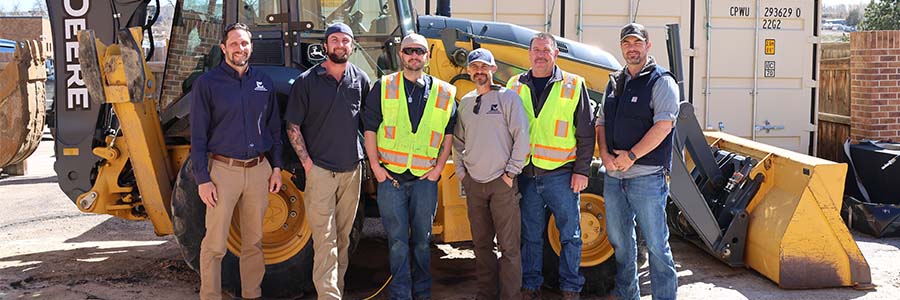 Group of men standing in front of a backhoe